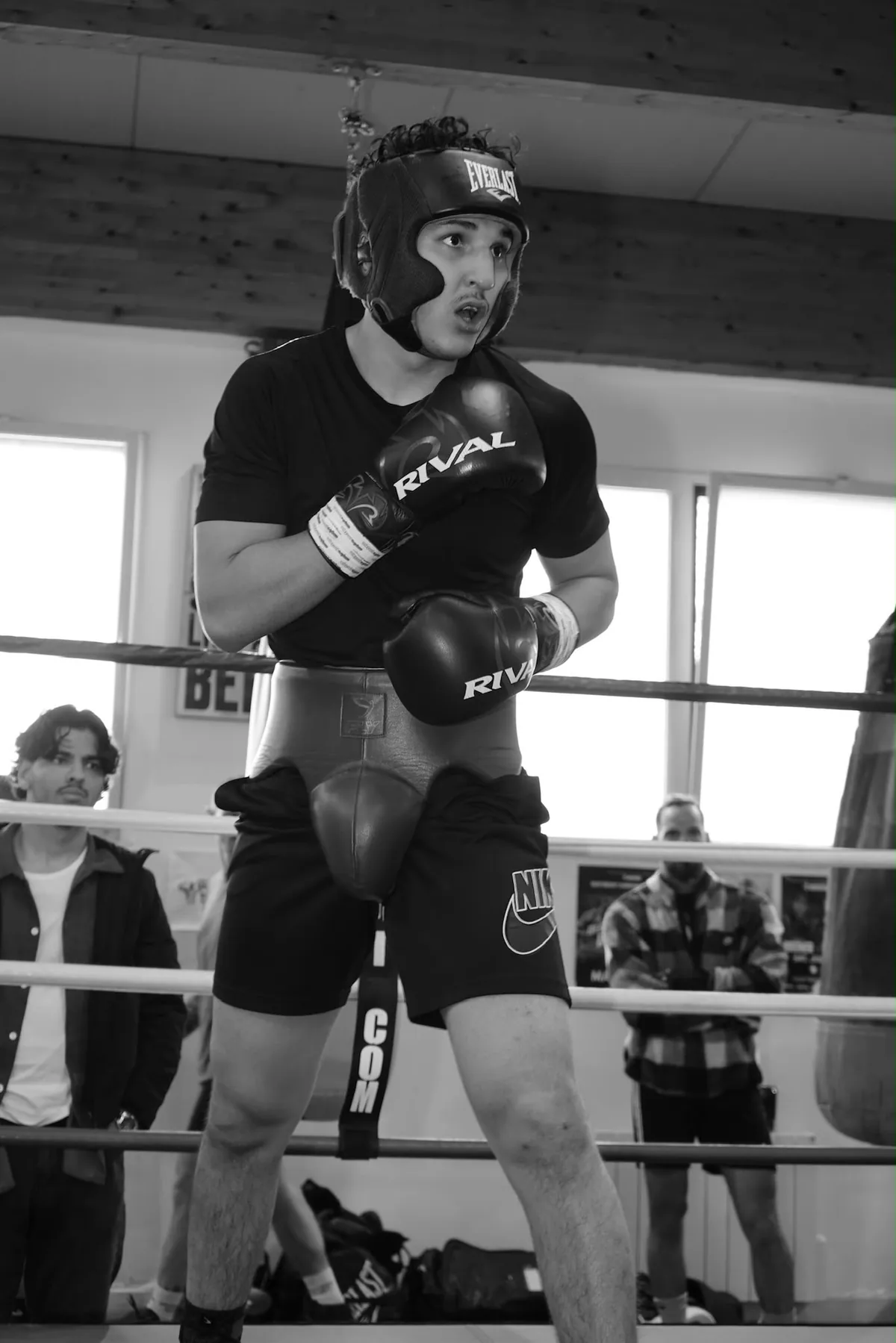 Photographie en noir et blanc d’un combattant casqué et ganté, en garde sur un ring.