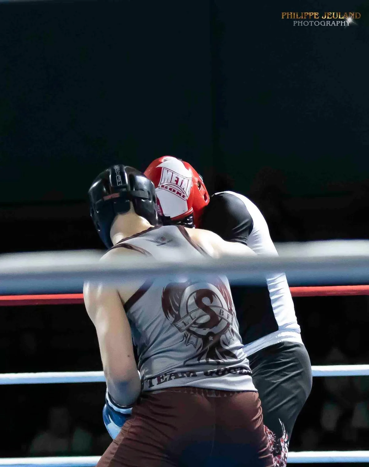 Yann Laurent au corps à corps avec son adversaire sur le ring, casques de protection et maillot de son club.
