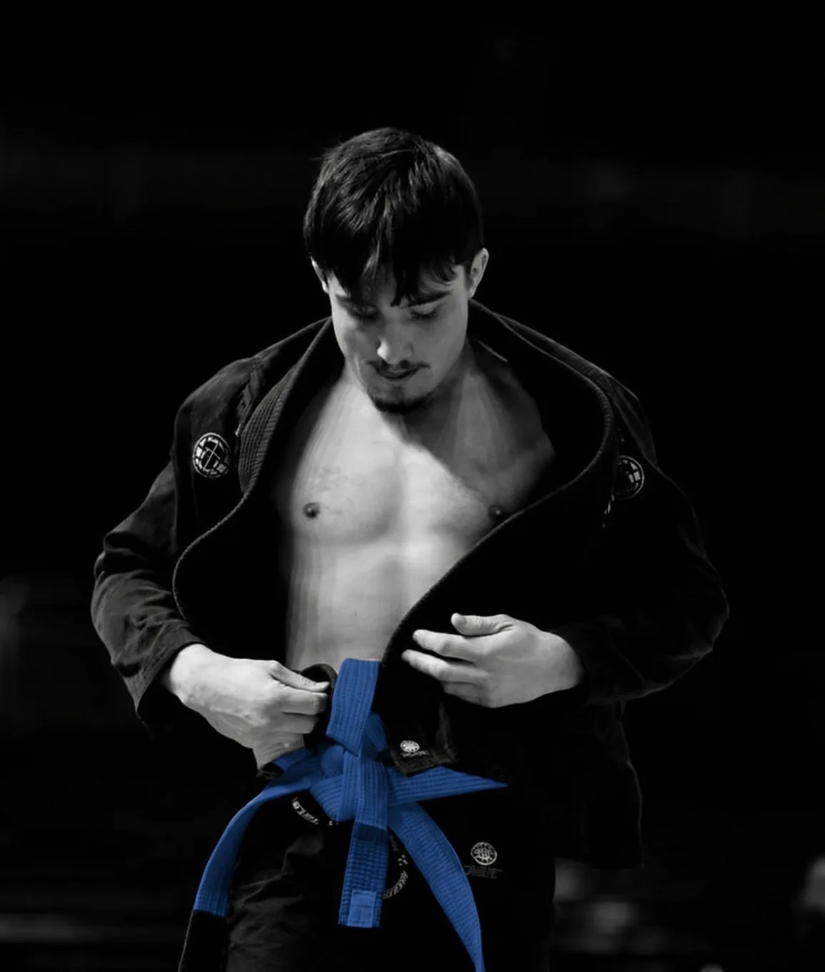 Combattant de jiu-jitsu brésilien ajustant sa ceinture bleue, kimono noir ouvert.