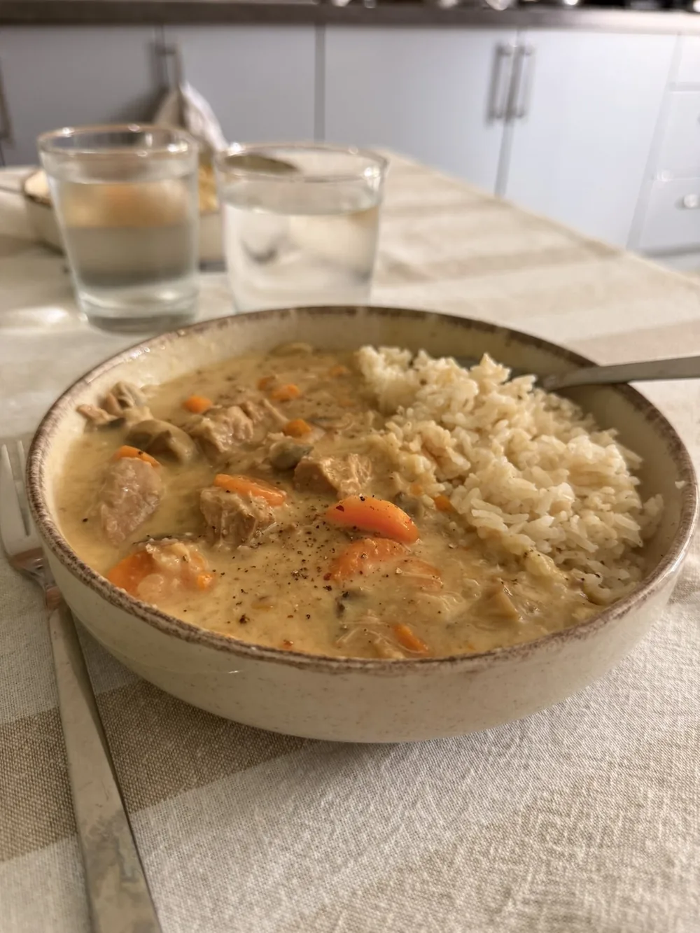 Bol de blanquette de veau au riz et aux carottes, posé sur une table, avec deux verres d’eau.