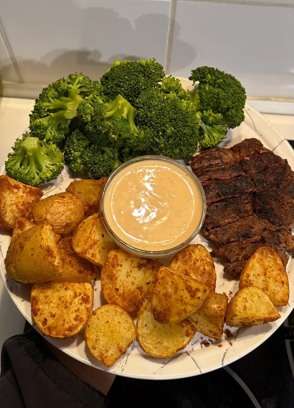 Assiette garnie de pommes de terre rôties, de brocolis vapeur, de viande grillée et d’un bol de sauce.